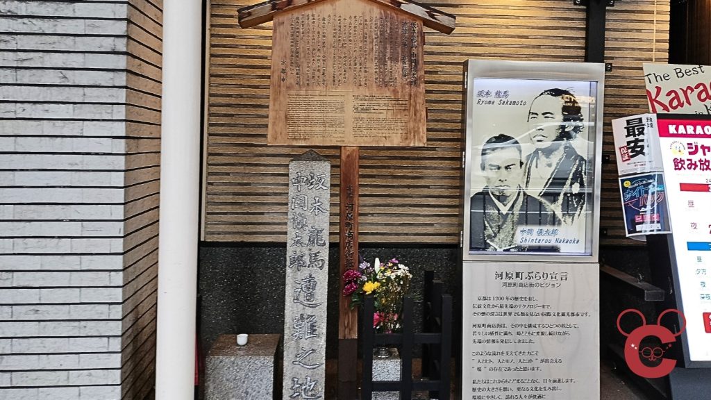 京都市中京区河原町通にある「近江屋跡」の石碑。「坂本龍馬 中岡慎太郎 遭難之地」と刻まれた石碑と、詳細な解説が書かれた案内板、二人の肖像写真パネルが並んでいる様子を正面から撮影した写真。中岡慎太郎ランドの史跡巡り解説用。