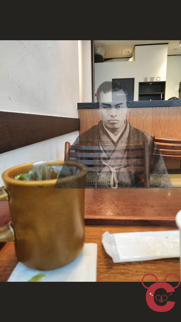 京都市中京区の「中岡慎太郎寓居跡」に建つカフェ「抹茶館」の店内風景。飲み終わった後の抹茶ラテのカップがある客席の椅子に、うっすらと半透明の姿で中岡慎太郎が座っている。歴史の面影を感じさせるエモーショナルな演出がされた中岡慎太郎ランドの記事用スライド。