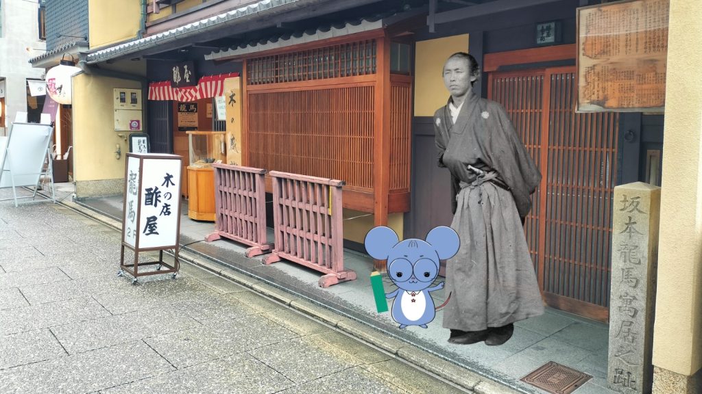 京都にある坂本龍馬の海援隊拠点「酢屋」の外観と、「坂本龍馬寓居之址」の石碑を紹介する画像。入り口前には坂本龍馬の肖像写真とネズミのキャラクター「ちゅう乃」が並んで立っている。中岡慎太郎ランドの史跡巡り記事用スライド。