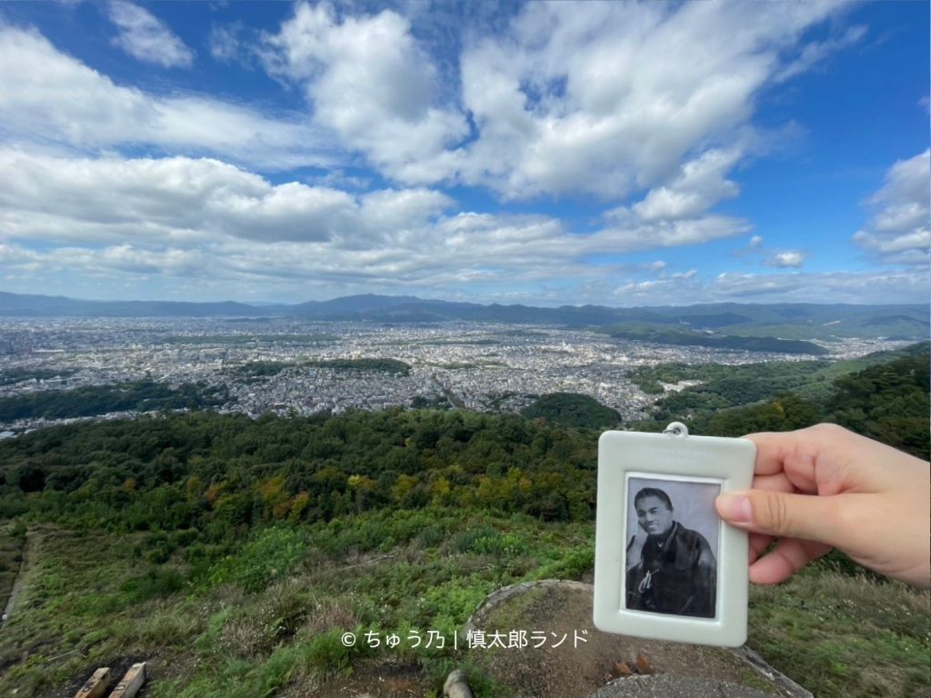 京都・大文字山の火床付近から望む京都市街の絶景と、手に持った笑顔の中岡慎太郎の写真入りキーホルダー。