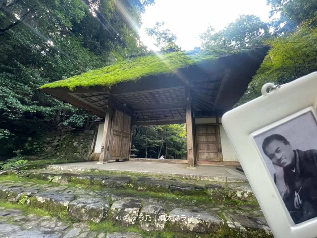 京都・法然院の苔むした茅葺屋根の山門と、手前に掲げた笑顔の中岡慎太郎の写真入りキーホルダー。