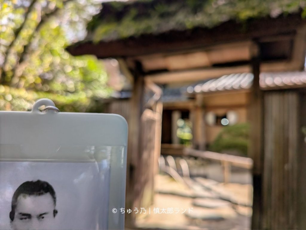 中岡慎太郎の写真入りキーホルダーを手前に掲げた写真。背景には京都・詩仙堂の木造の門がぼかして写っている。